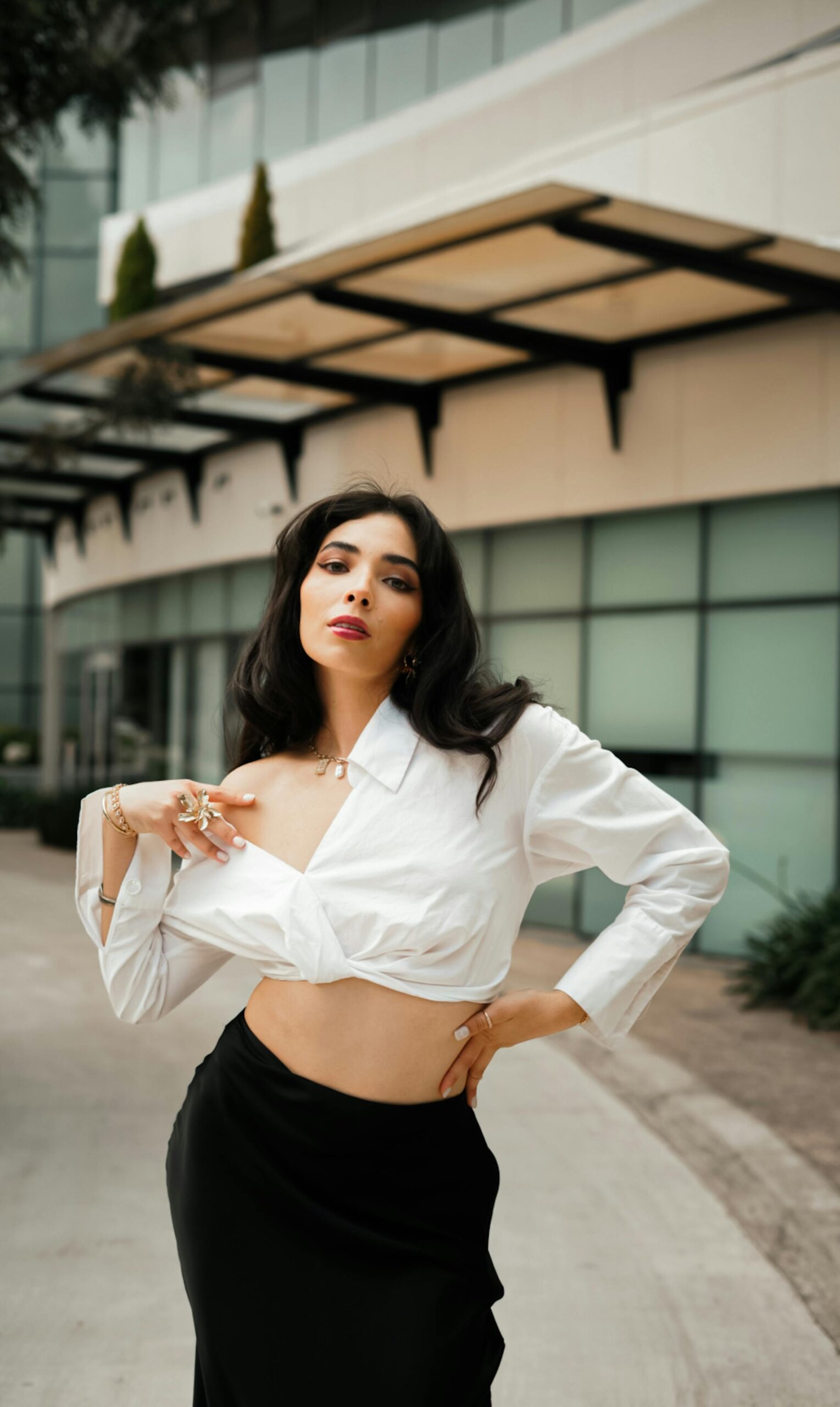 Fashionable woman posing confidently in an urban setting with modern architecture.